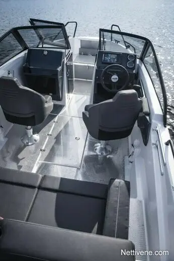 Interior view of a boat featuring two captain's chairs, steering console, and a sleek, metallic floor by calm water.